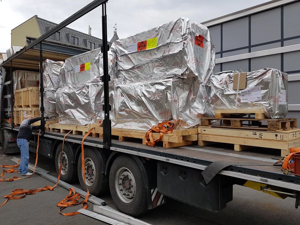 Verpackte Druckmaschinenkomponenten, gesichert auf einem Transportauflieger.